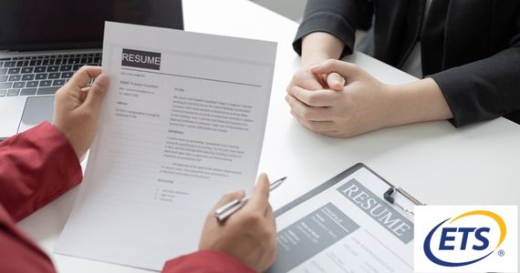 Person holding a resume with both hands and a pen and another person with hands folded on the table, ETS logo